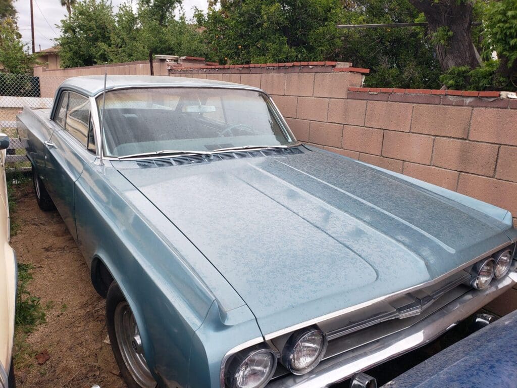 Vintage blue classic car parked beside a brick wall.
