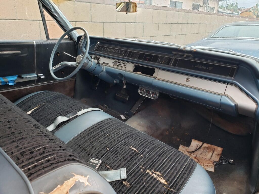 Interior of an old, worn-out car with damaged seats and a simple dashboard.