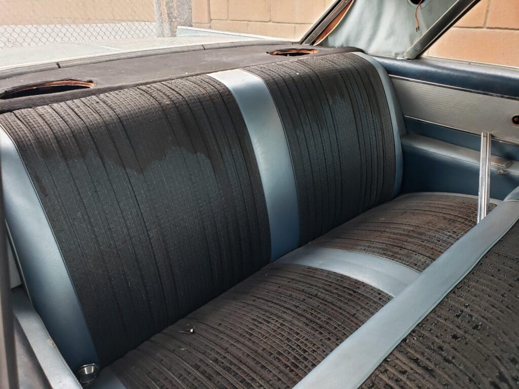 Vintage car interior with a classic black bench seat and seatbelt.