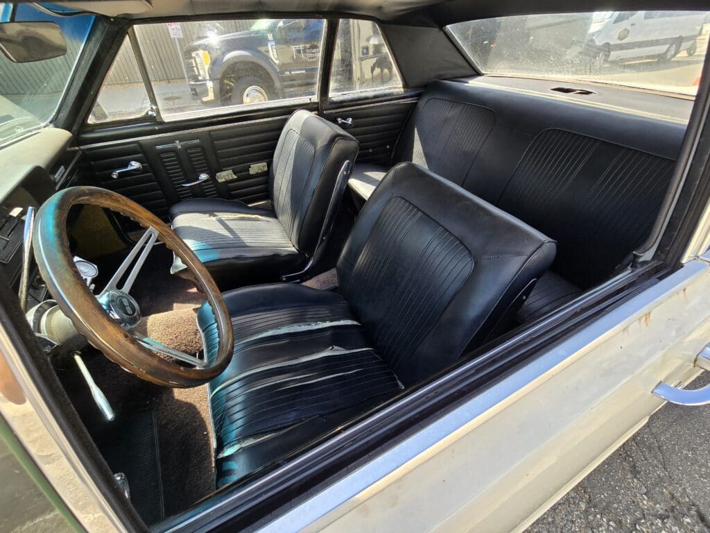 Classic car interior with vintage black leather seats and wooden steering wheel.
