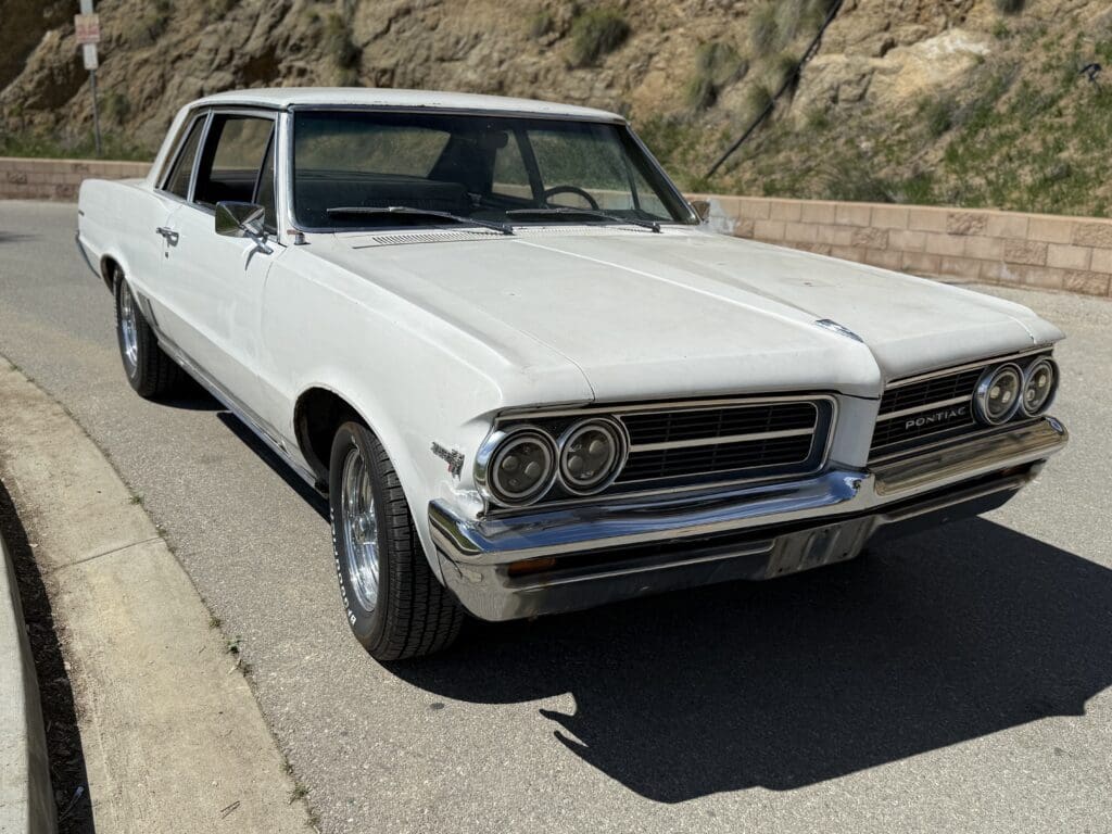 Classic white muscle car parked on a sunny mountain road.
