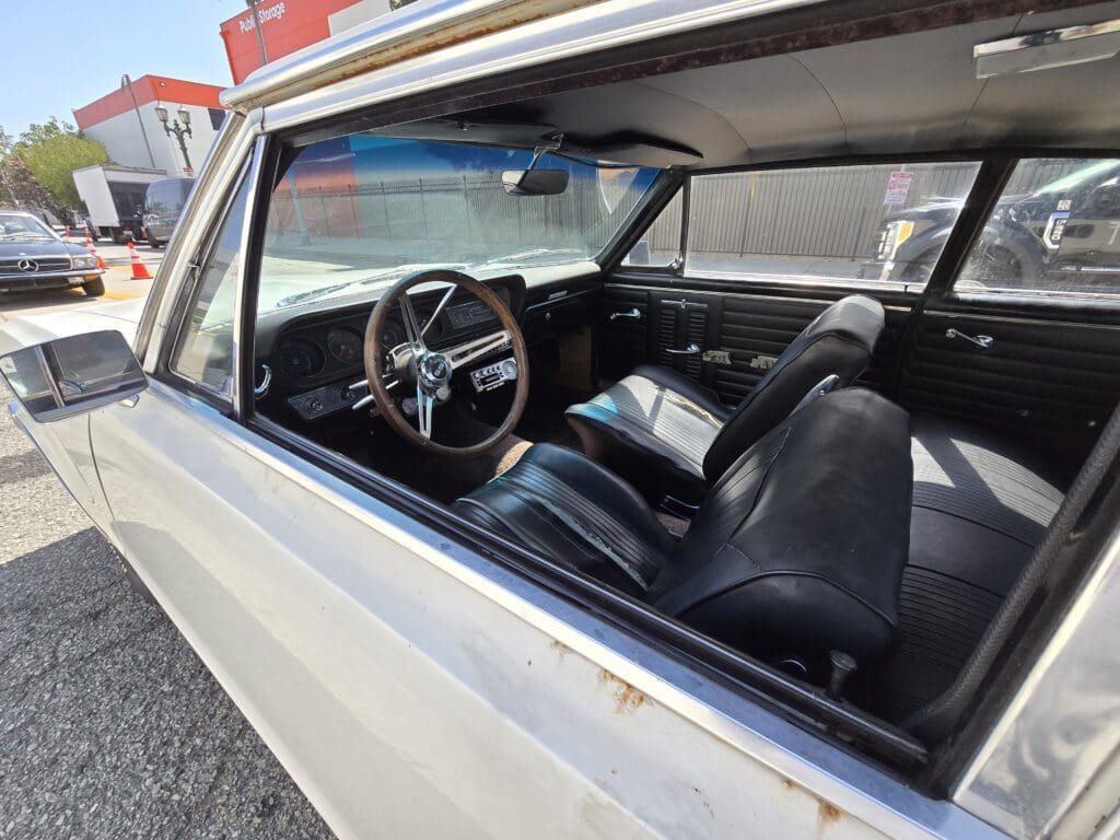 Interior view of a classic car with black leather seats and a vintage steering wheel.