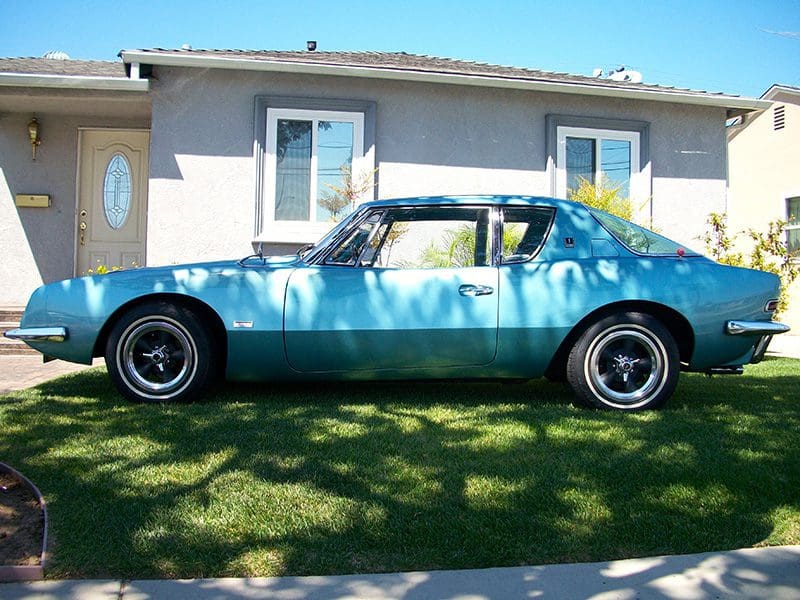 Classic blue muscle car parked on grass in front of a house.