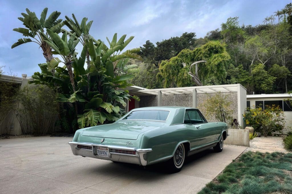 Classic green vintage car parked by a tropical garden.