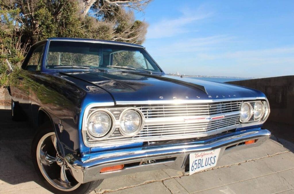 Classic blue vintage car parked by the seaside under clear skies.