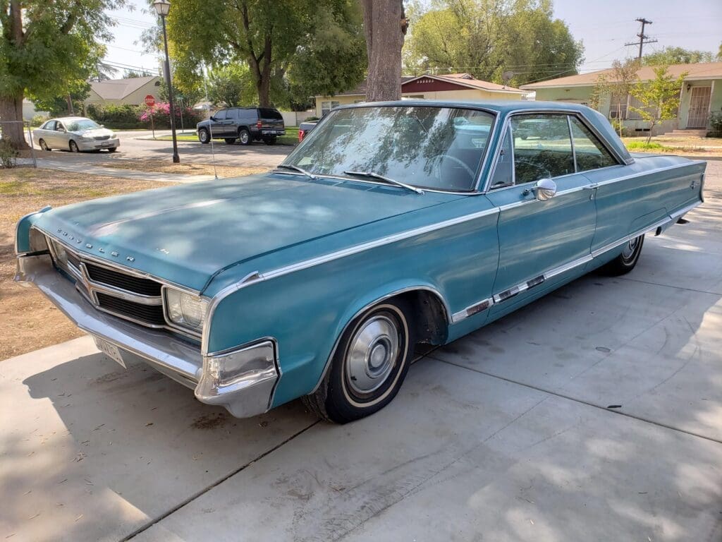 A vintage blue Pontiac car parked on a driveway under trees.
