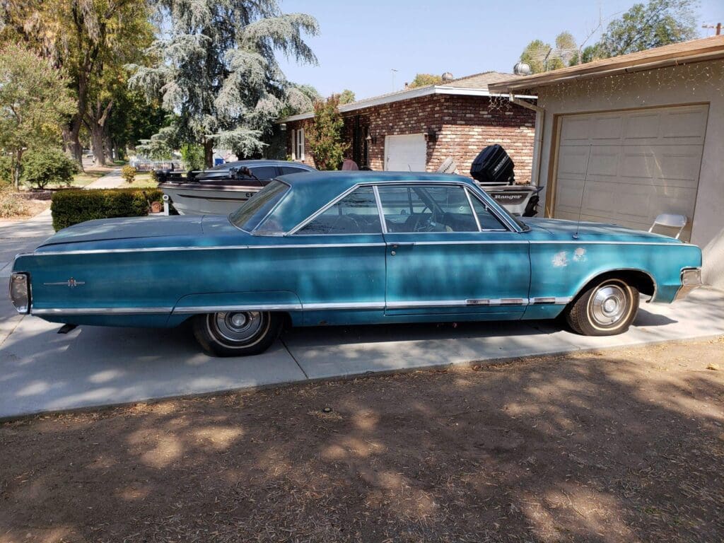 Vintage blue car parked in a sunny driveway beside a house.