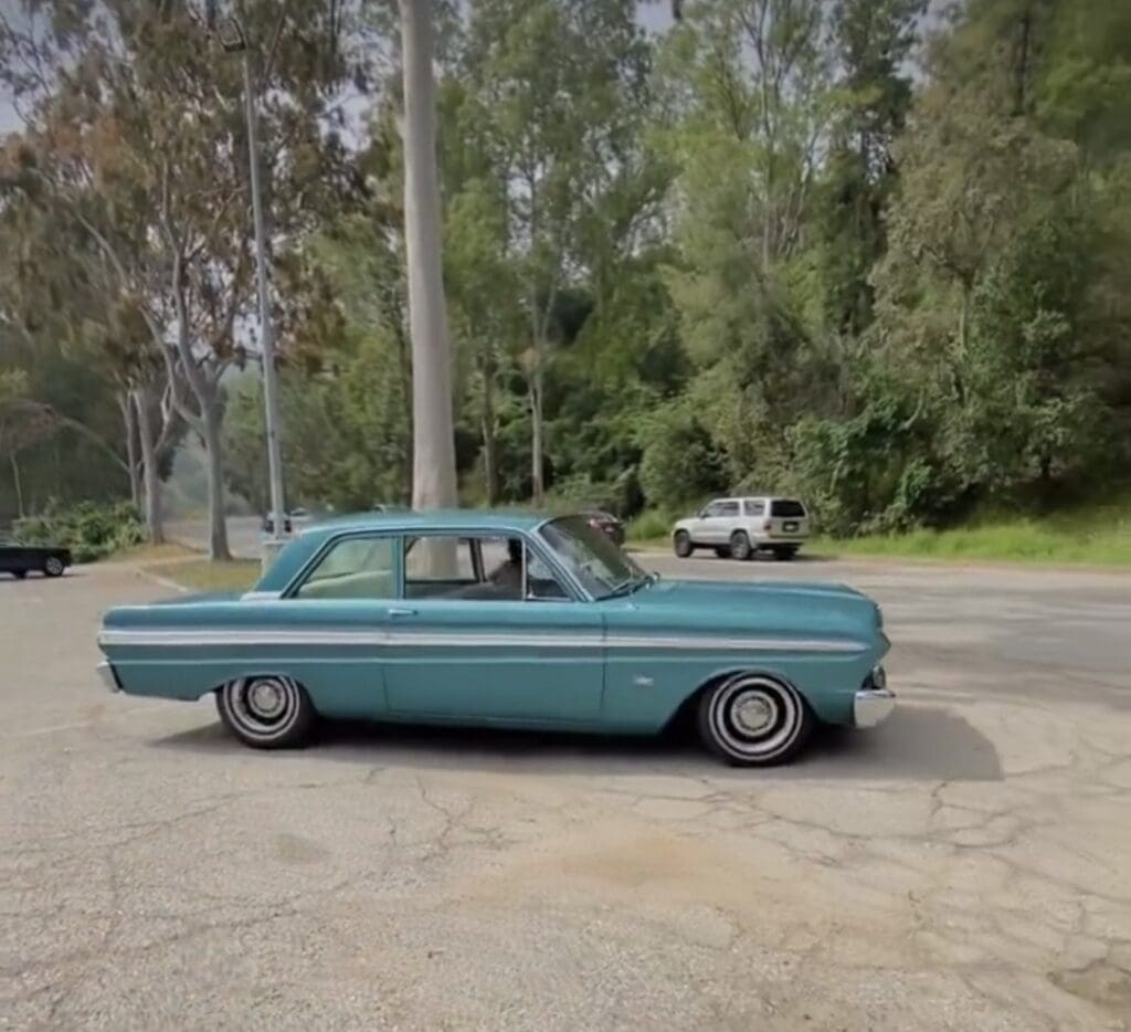 A vintage blue car parked on a concrete surface near trees.