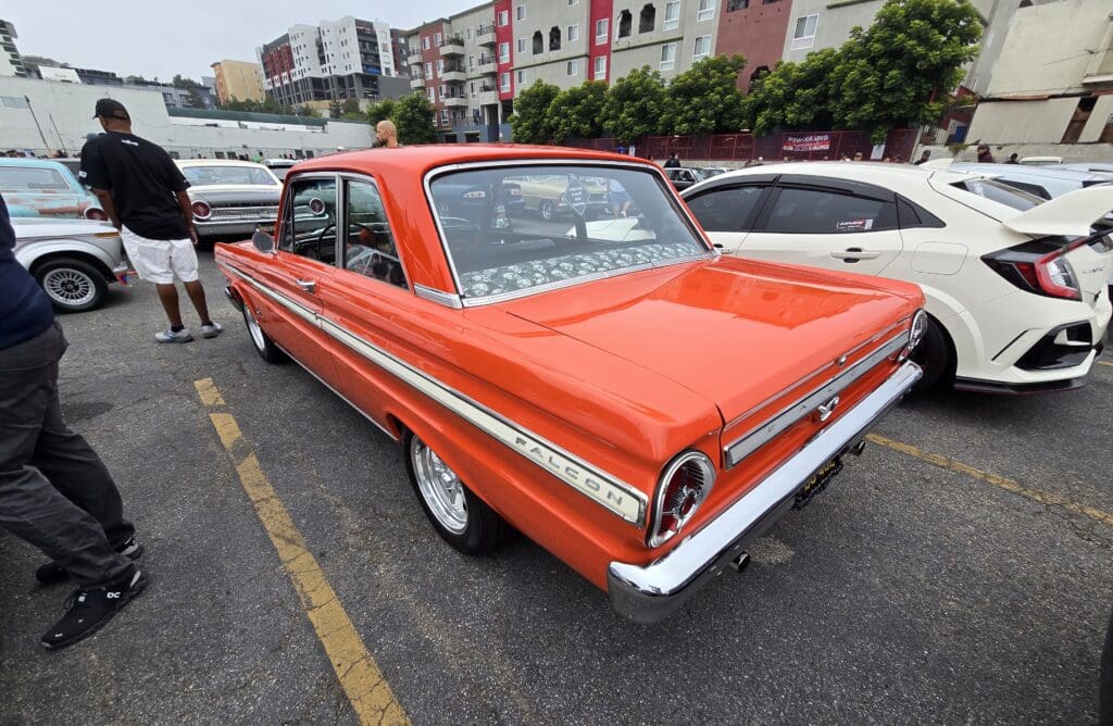 Classic orange Ford Falcon parked in a busy lot.