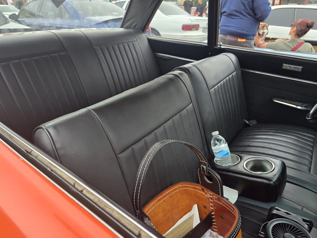Interior of a vintage car with black leather seats and a picnic basket.