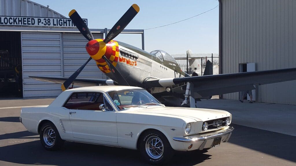 Classic white Ford Mustang parked in front of a vintage aircraft.