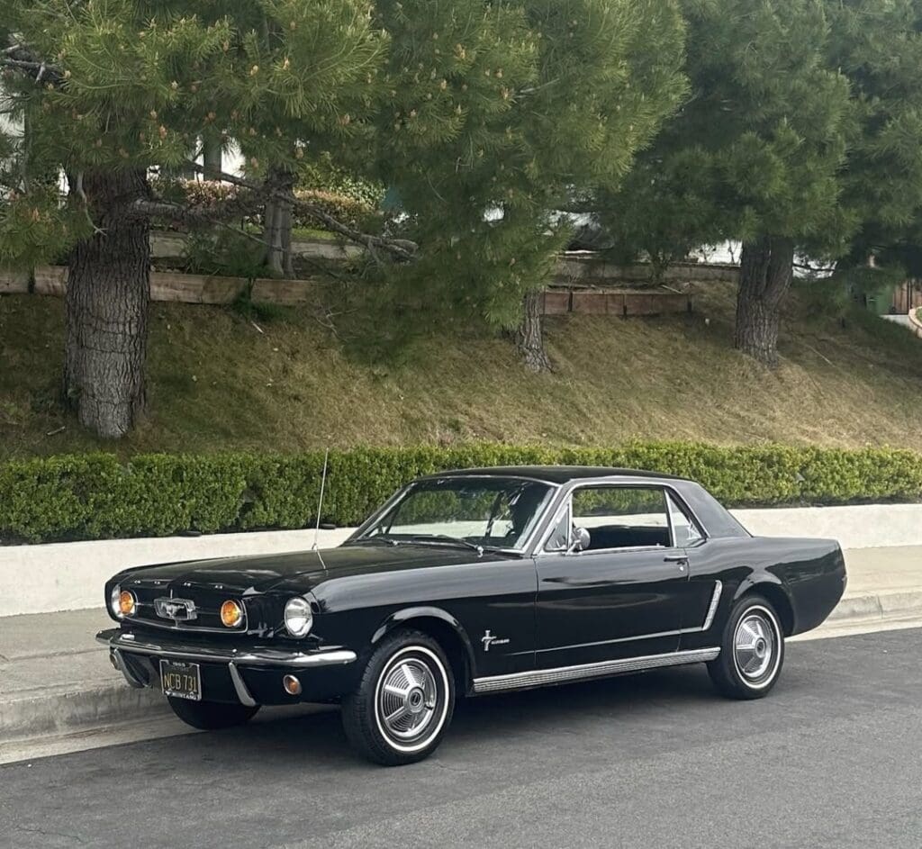 Classic black vintage car parked on a street with trees in the background.