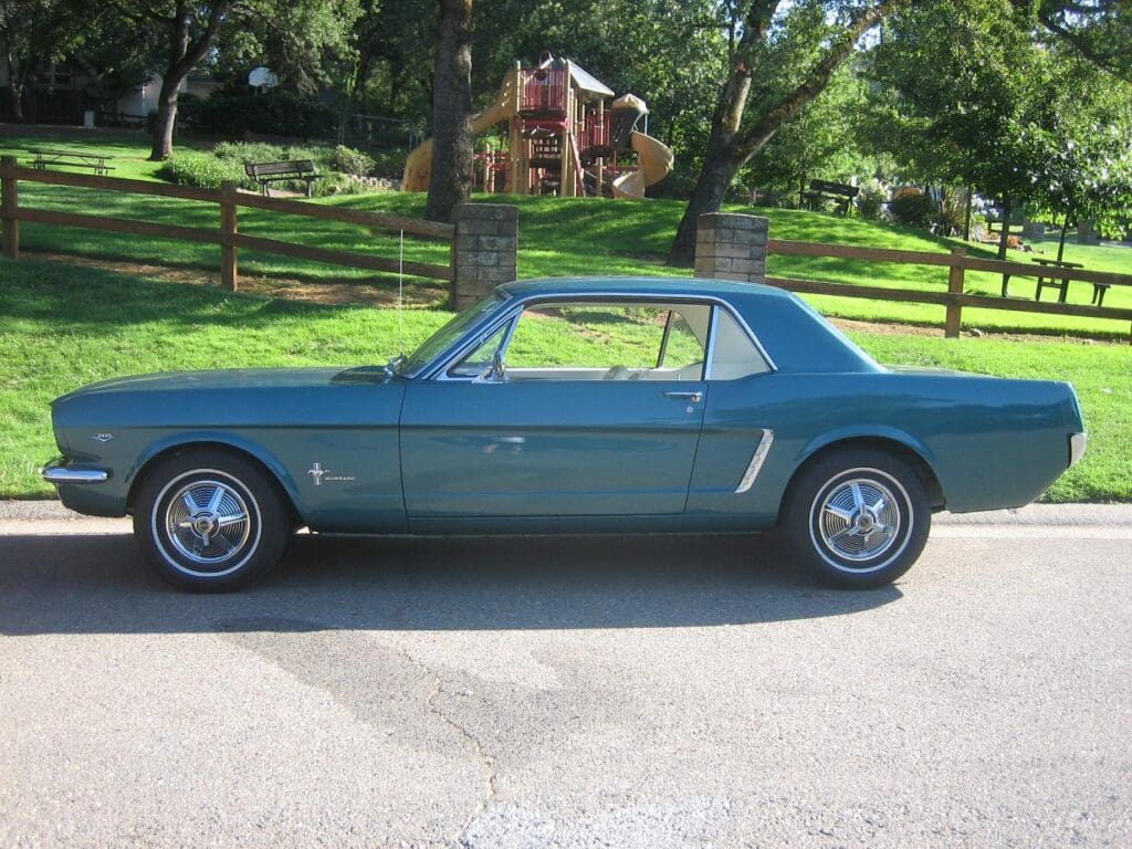 Classic blue convertible car parked on a driveway with a wooden fence and house in the background.