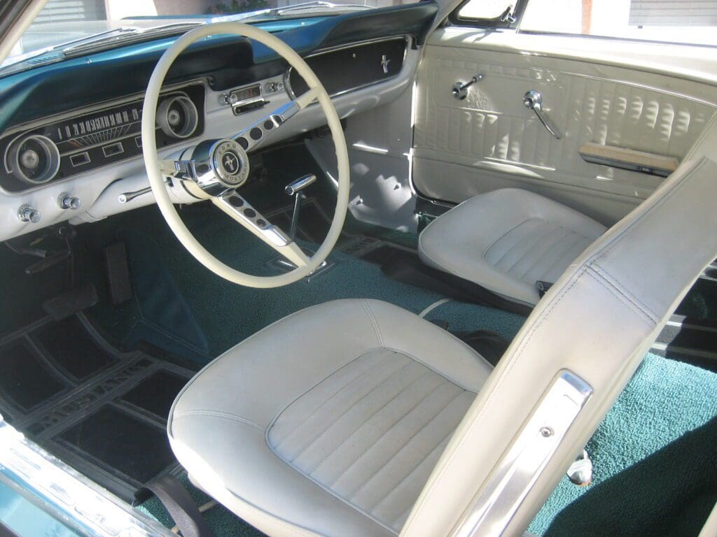 Interior of a classic car with white seats and steering wheel.
