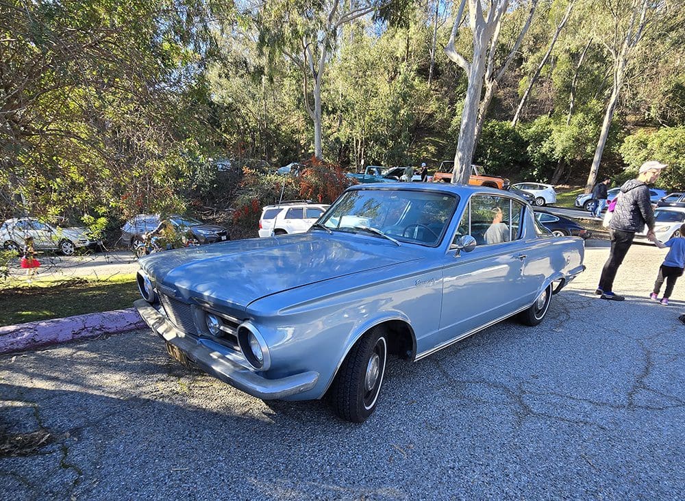 Classic light blue coupe parked beside a curb with trees in the background.