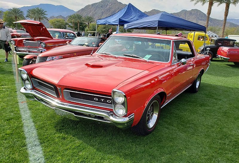 Classic red Pontiac GTO parked on grass at a car show.