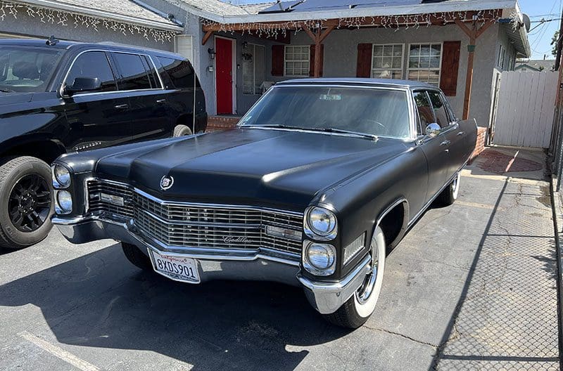Classic black Cadillac parked in a driveway beside a modern SUV.