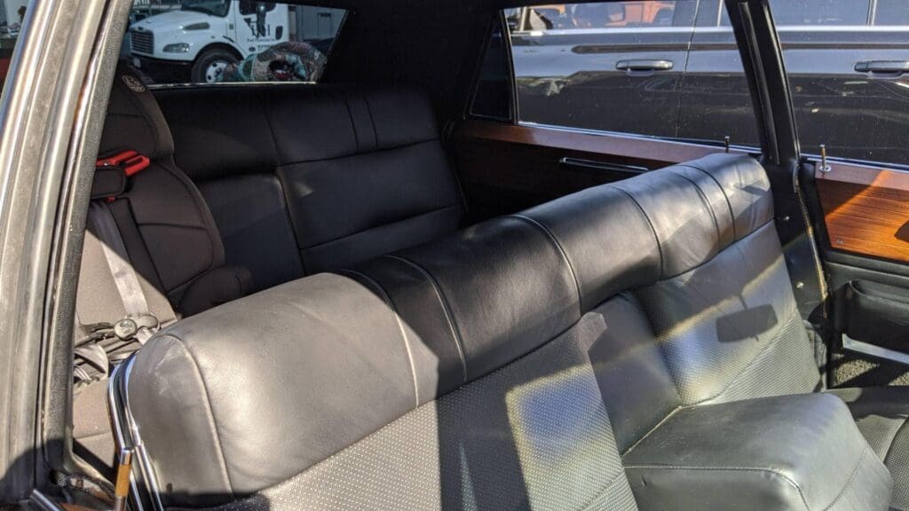 Luxurious black leather backseat of a classic car with wood trim.