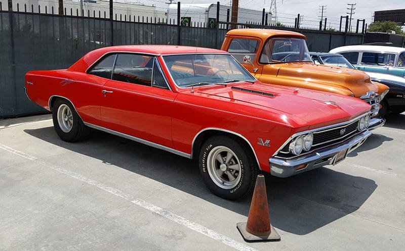 Red vintage muscle car parked next to an orange truck.