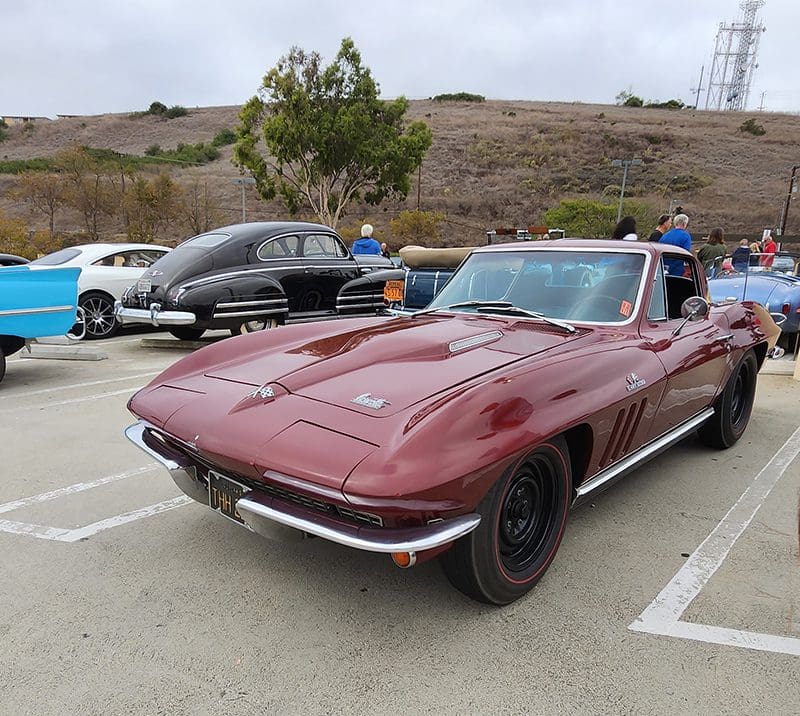 Vintage red Corvette parked in a lot with other classic cars.
