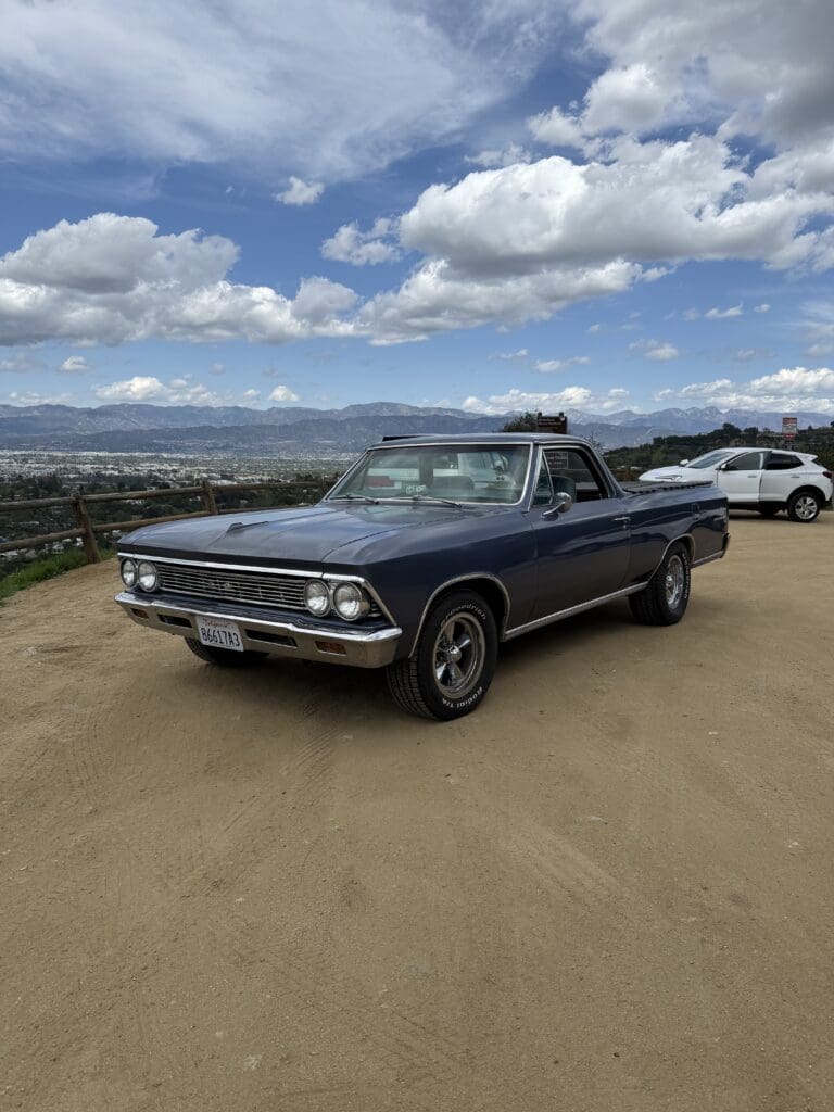 Classic vintage car parked on a scenic hill under blue skies.