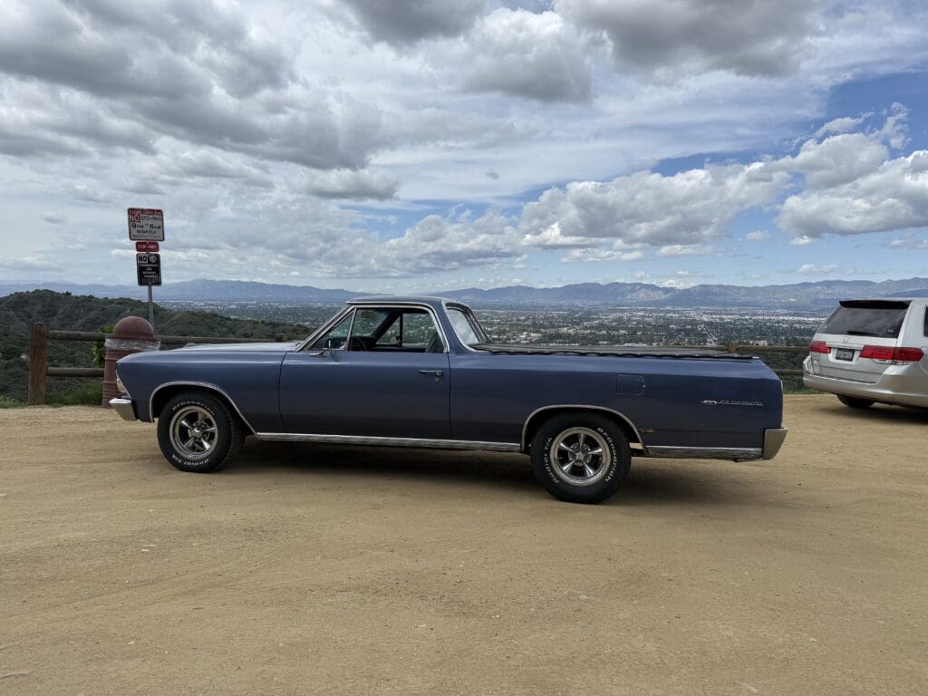 Classic blue Chevrolet El Camino parked on a hill with a cloudy sky.