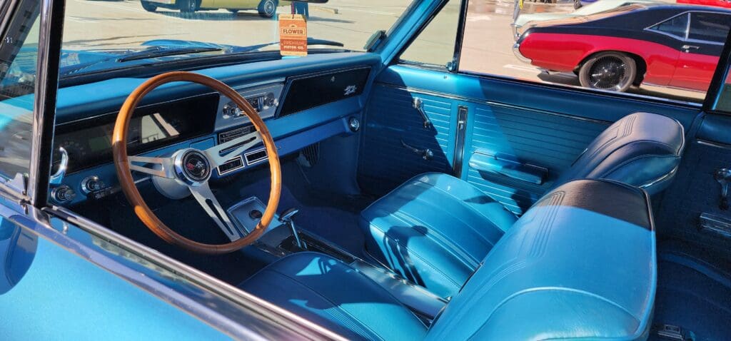 Classic car interior with turquoise upholstery and wooden steering wheel.