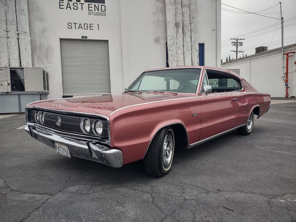 Classic red muscle car parked near a vintage studio building.