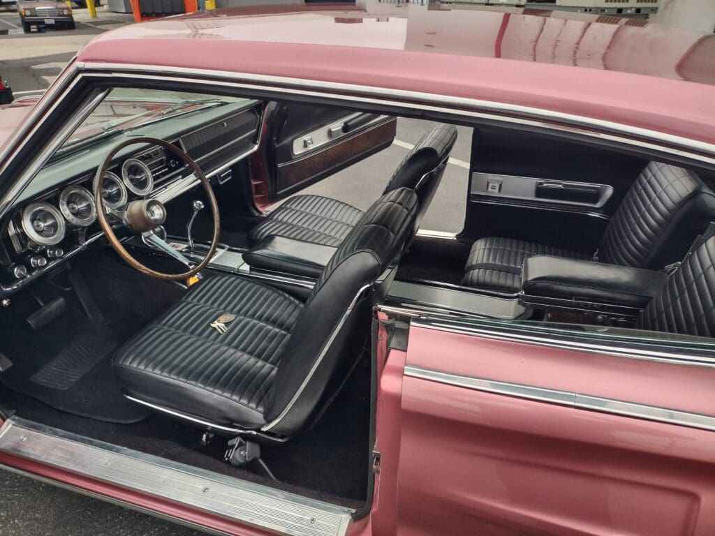 Interior view of a classic pink car with black seats and vintage dashboard.