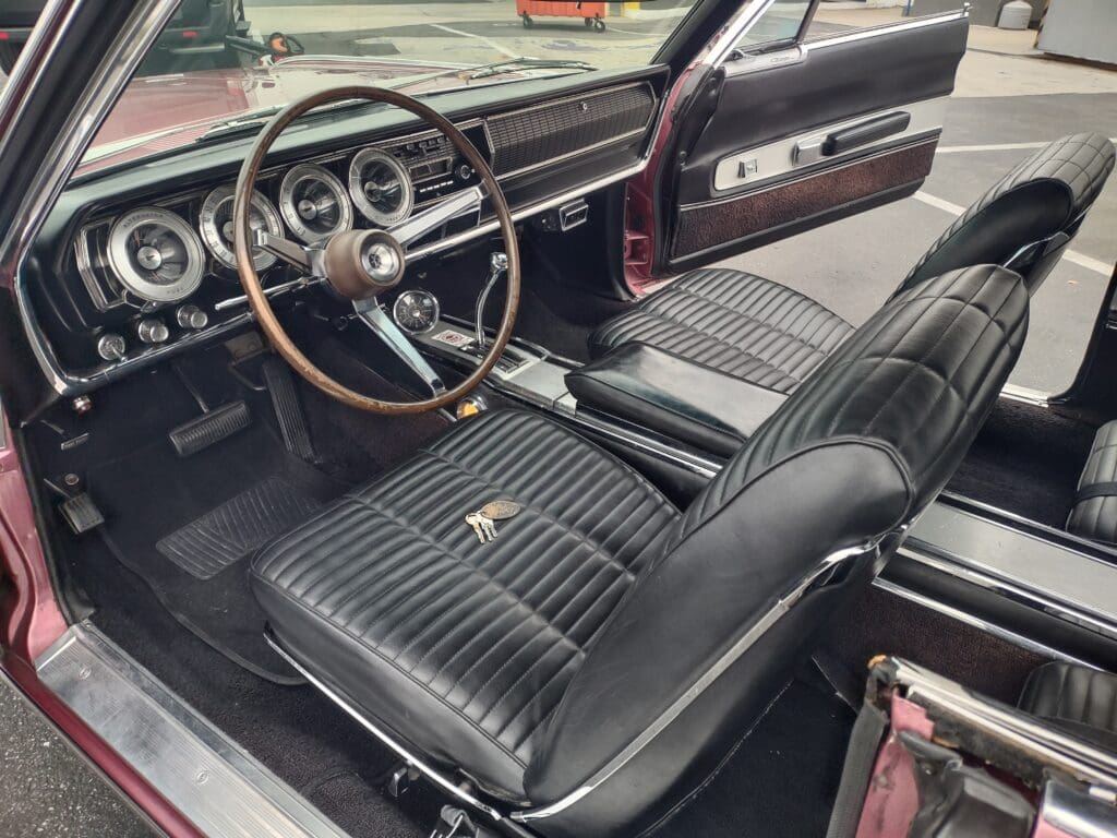 Classic car interior with black leather seats and wooden steering wheel.