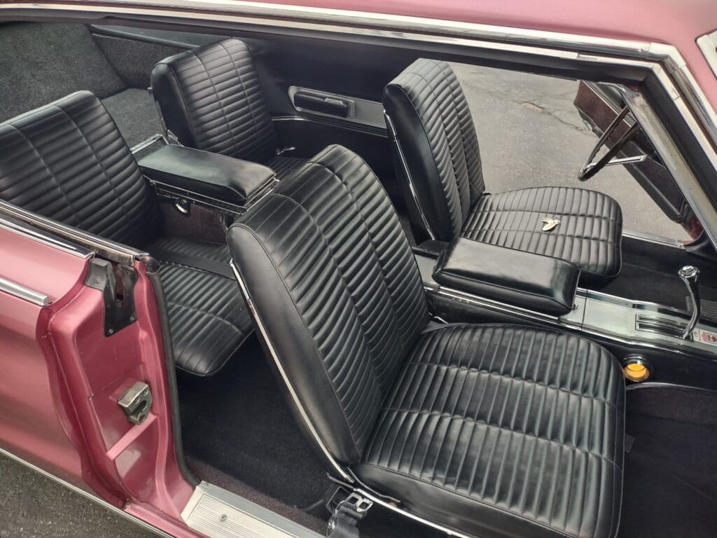 Interior view of a classic car with black vinyl seats and a pink door frame.