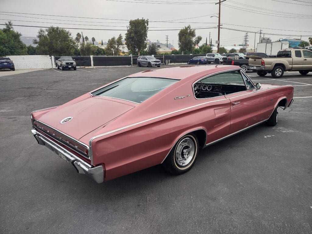 A vintage pink muscle car parked on asphalt under cloudy skies.