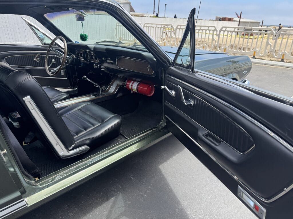 Classic dark green convertible Mustang parked outdoors on a sunny day.