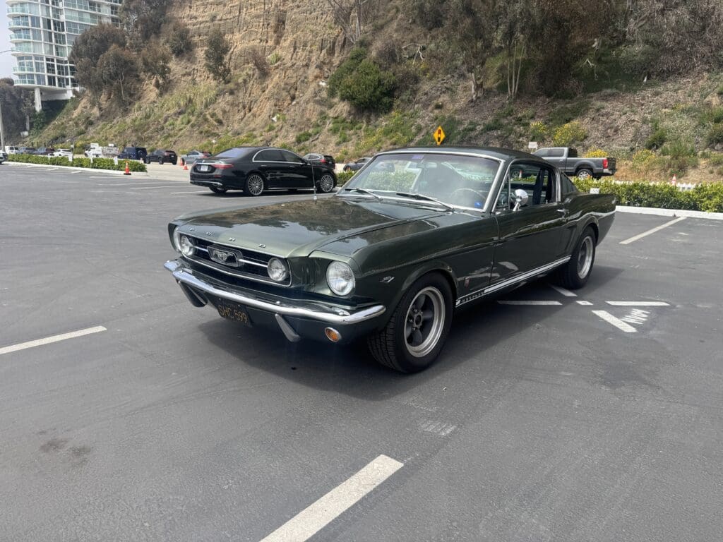 Classic green convertible car parked outdoors with scenic rocky background.