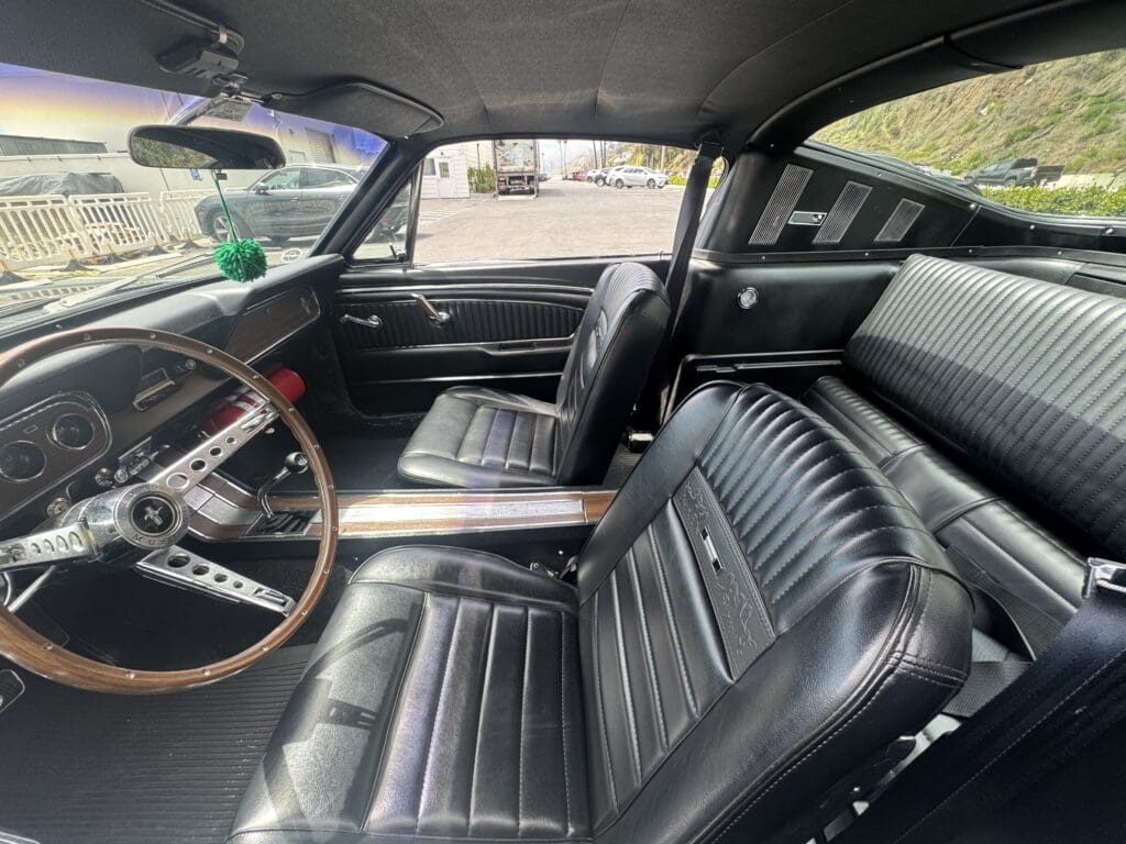 Interior of a classic car with black leather seats and wooden steering wheel.