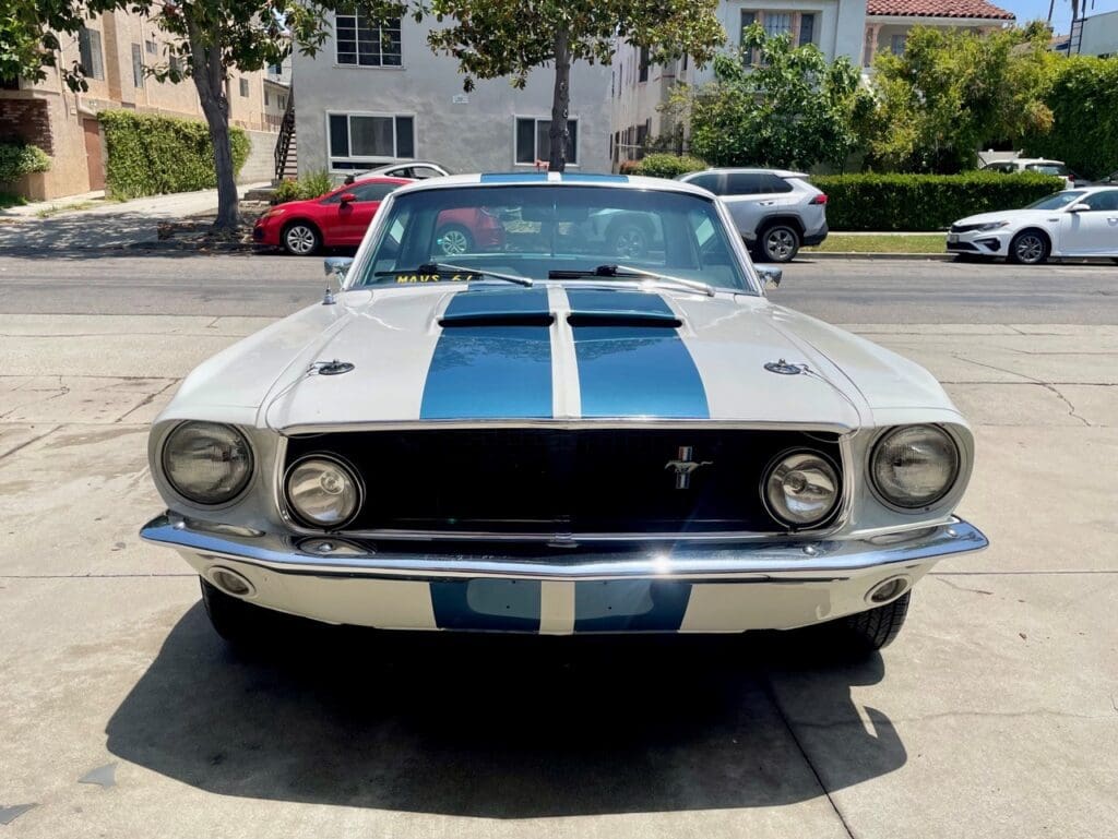 Classic white Ford Mustang with blue racing stripes parked outdoors.