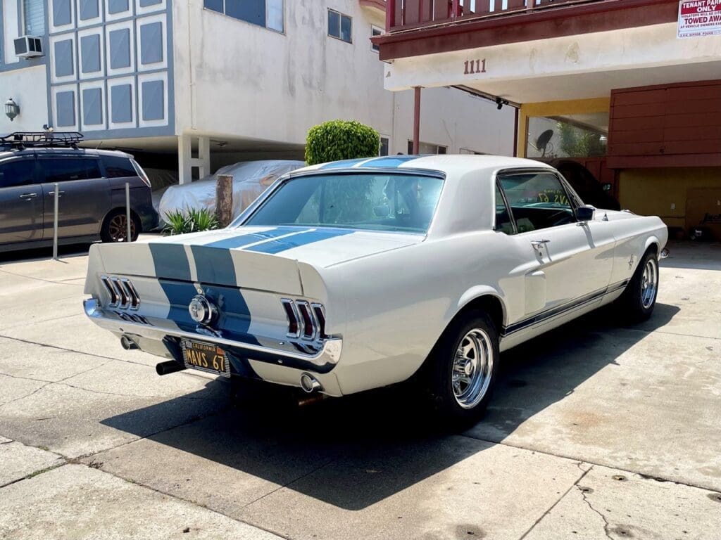 Classic white Ford Mustang with blue racing stripes parked outdoors.