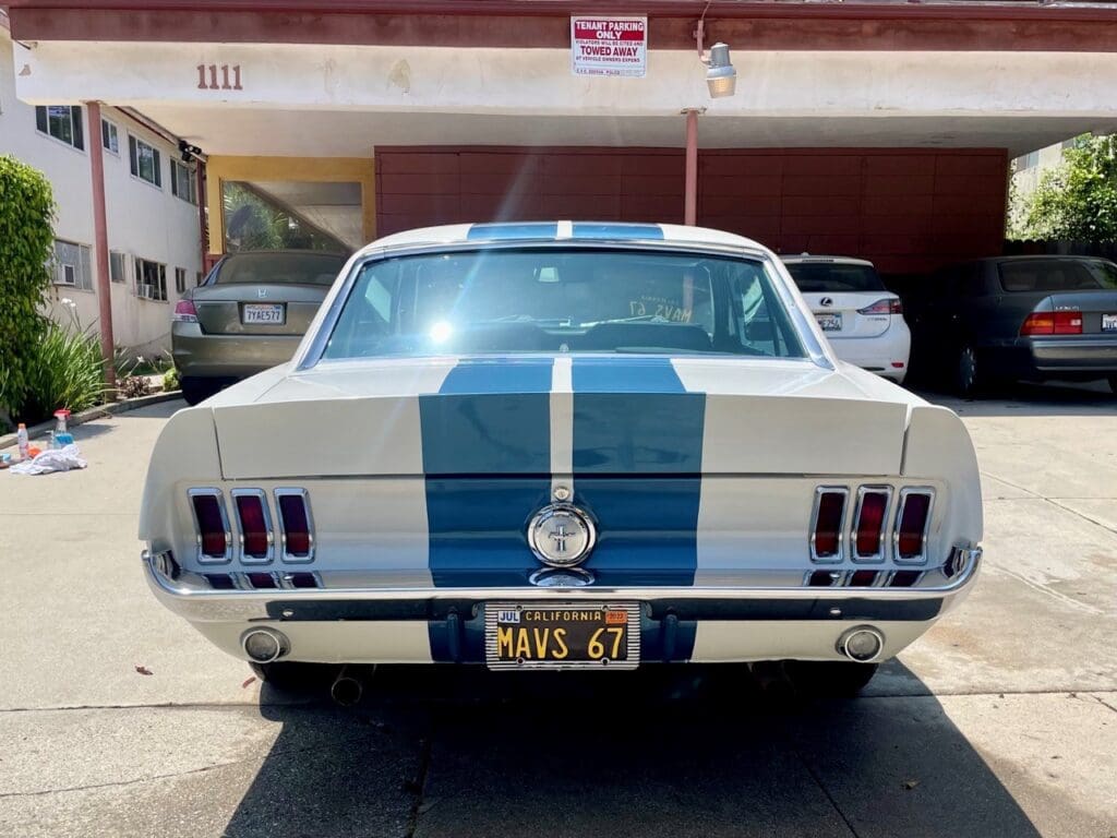 Classic white Ford Mustang with blue racing stripes parked outdoors.