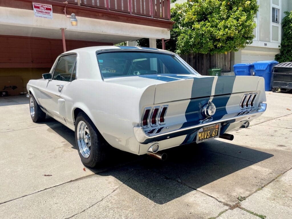Classic white Ford Mustang with blue racing stripes parked outdoors.