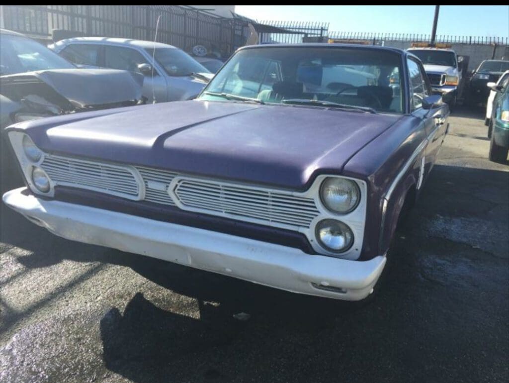 Classic vintage purple car with chrome detailing parked outdoors.
