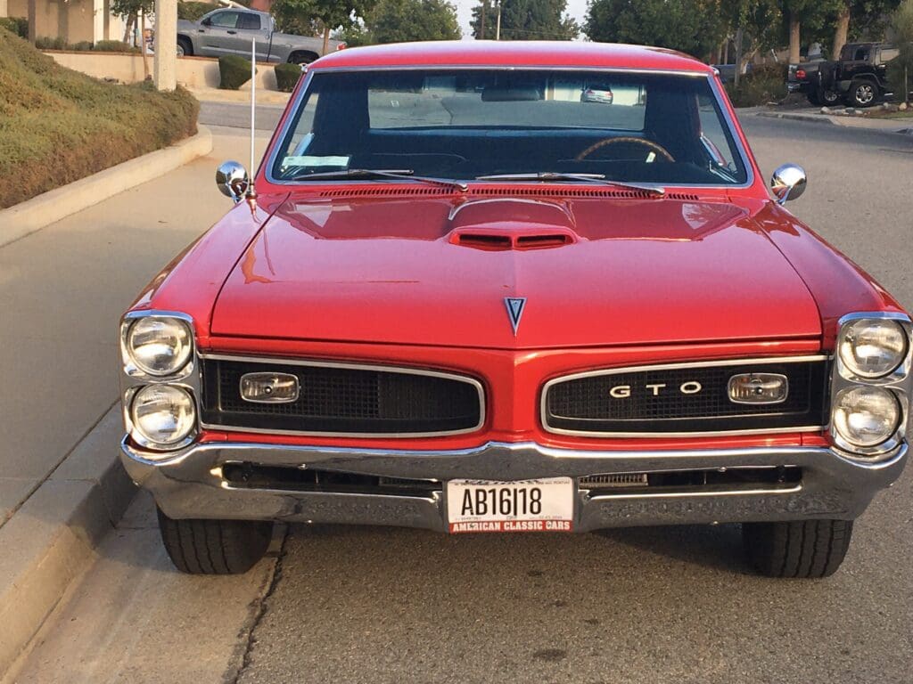 Front view of a classic red Pontiac GTO with a hood scoop.