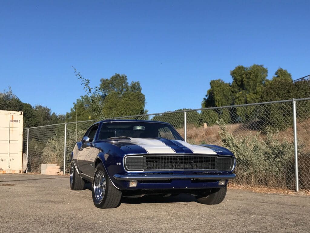 Classic blue muscle car with white racing stripes parked outdoors under clear sky.