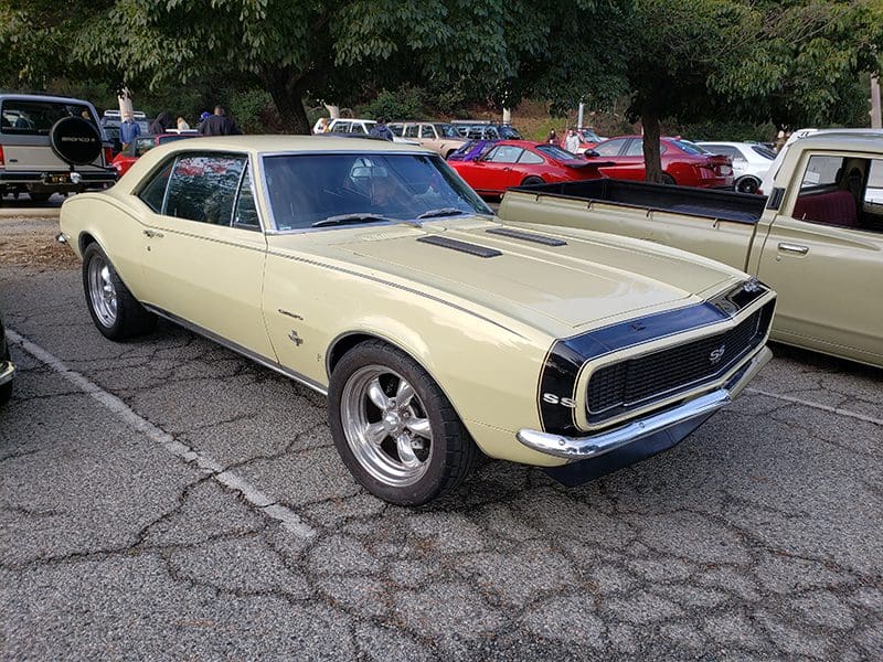 Classic yellow muscle car parked outdoors at a car show.
