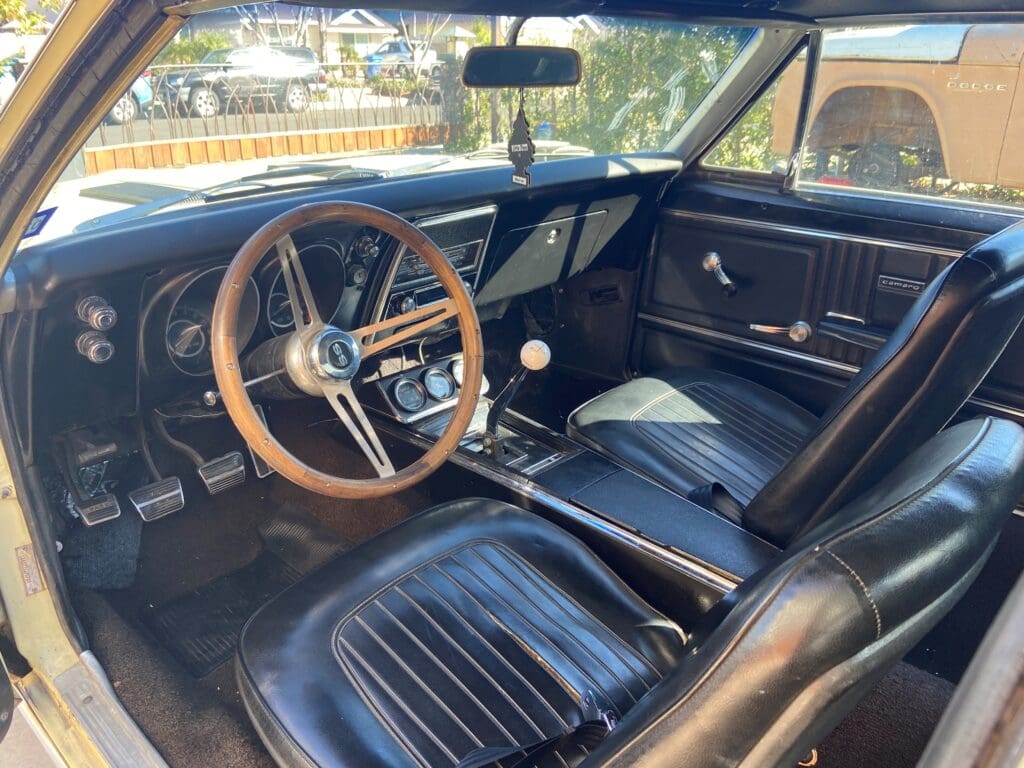Interior of a classic car with a wooden steering wheel and black leather seats.