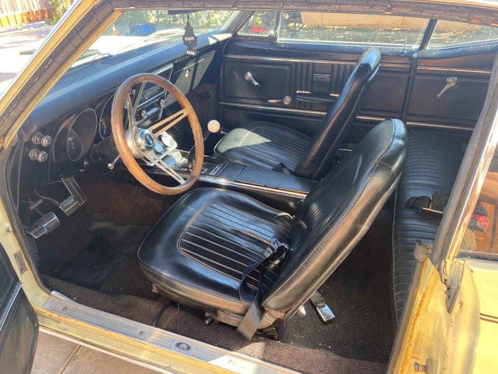 Classic car interior with wooden steering wheel and black leather seats.