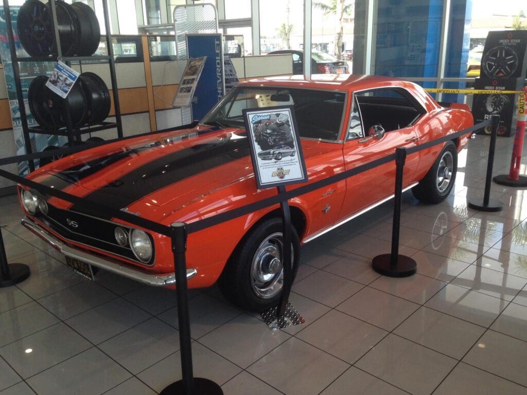 Orange and black vintage muscle car displayed indoors with informational sign.