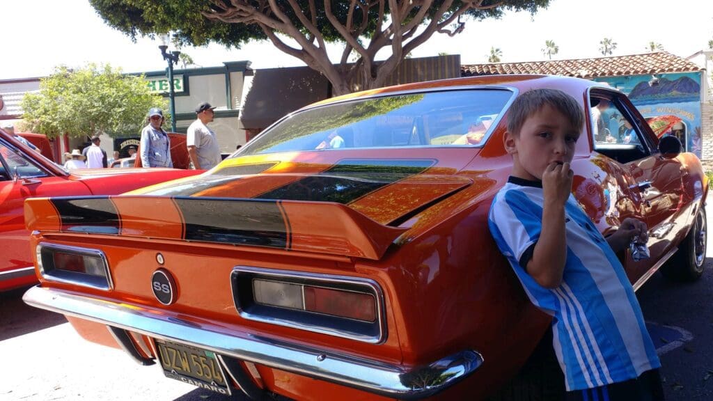 Bright orange classic car with a black stripe and spoiler at a car show.