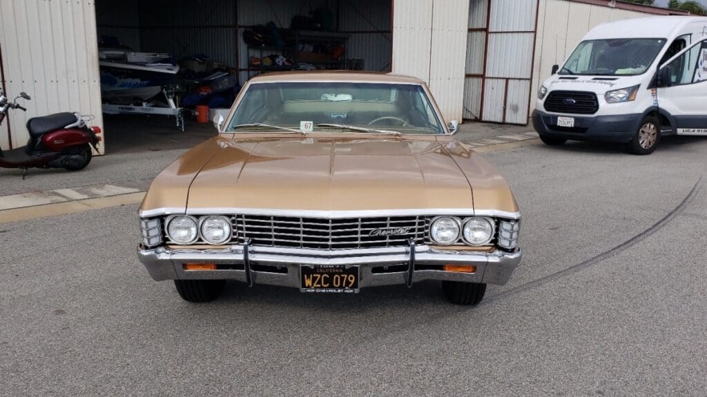Classic beige vintage car parked outside a garage.
