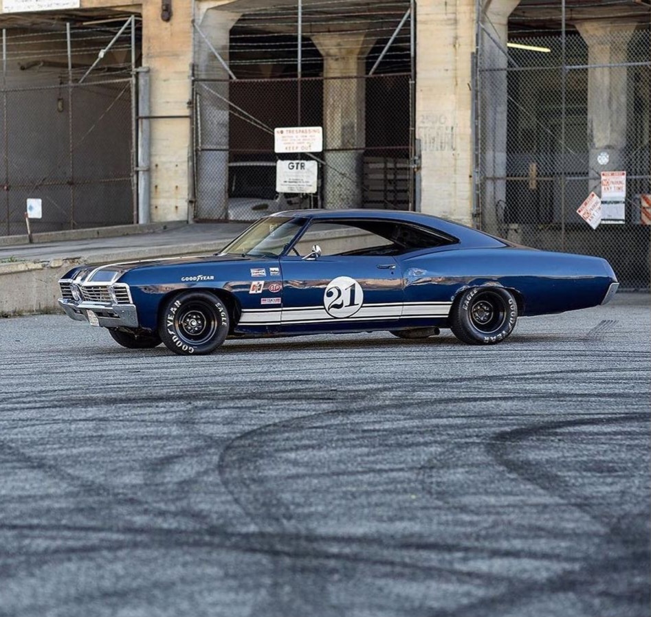 Classic blue muscle car parked near an old building with tire marks on the ground.