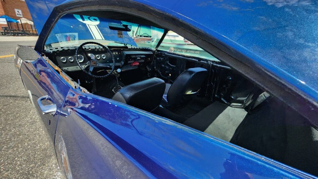 Classic blue muscle car parked near an old building with tire marks on the ground.